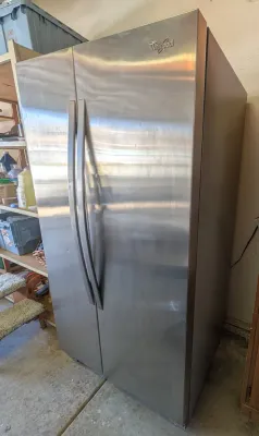 Whirlpool side-by-side refrigerator in a stainless steel finish, featuring curved handles and a clean exterior.