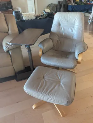 Scandinavian-style swivel recliner and matching ottoman in grey leather with light wood bases, shown alongside an adjustable overbed table.