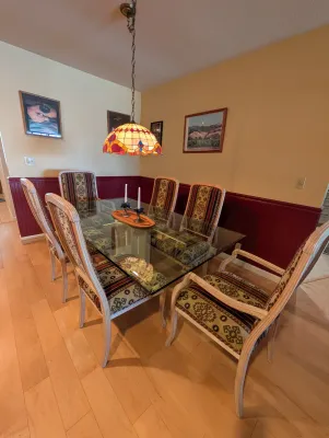 Contemporary glass-top dining table with a light wood frame, paired with six matching upholstered chairs featuring a southwestern-style...