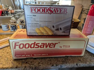 Vintage FoodSaver by Tilia vacuum packaging system in its original box, topped with a four-pack of VacLoc bags.