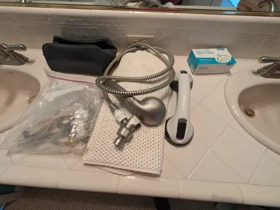 Assorted bathroom safety and utility items, including a handheld shower head with hose, a suction-cup grab bar, and a box of alcohol prep...