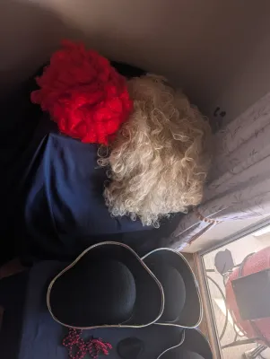 Assorted costume accessories, including a bright red curly wig, a blonde curly wig, and two black tricorn hats with silver trim.