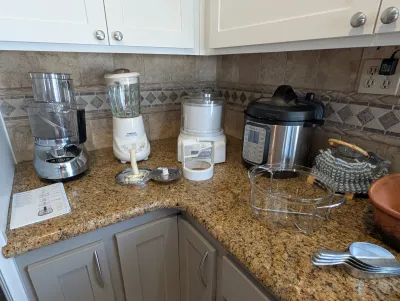 Collection of kitchen appliances on a granite countertop, including a Cuisinart food processor, a Cuisinart blender, an ice cream maker,...