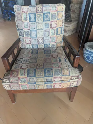 Mid-century modern style armchair featuring a dark wood frame with open-slat armrests and thick cushions upholstered in a multi-colored...
