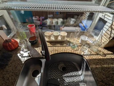 Assorted glassware, ceramic planters, and decorative items arranged on a granite countertop behind a kitchen sink.
