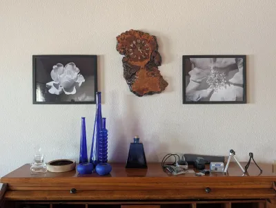 Vintage live-edge burl wood wall clock flanked by two framed black and white floral prints, displayed above a wooden desk with blue glass...