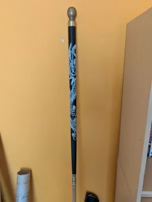 Black wooden walking cane featuring a white etched dragon design and a brass ball handle.