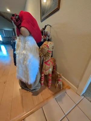 Large fabric Christmas gnome figure with a red hat and white faux fur beard, standing next to two traditional Scandinavian straw Yule...