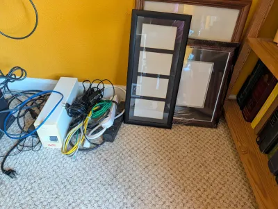 Assorted picture frames, including a black multi-photo collage frame, alongside an APC uninterruptible power supply and various power and...