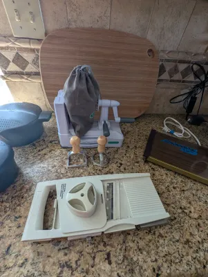 Pampered Chef mandoline slicer, spiralizer with storage bag, and various kitchen utensils displayed on a granite countertop.