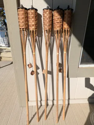 Set of five classic bamboo tiki torches with woven baskets and attached snuffer caps, showing light outdoor wear.