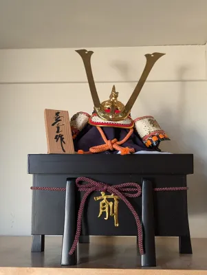 Japanese Boys' Day miniature samurai helmet (kabuto) display, featuring a detailed helmet with gold-tone horns, fabric accents, and...
