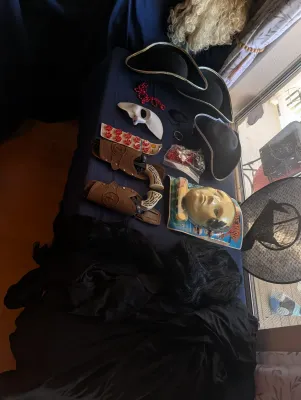 Assortment of Halloween and costume accessories, including pirate hats, toy cap guns with holsters, masks, and wigs displayed on a table.