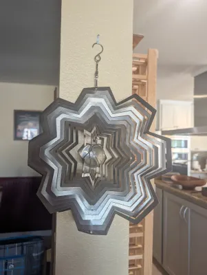 Hanging metal wind spinner with a multi-layered star design and a central glass marble accent.
