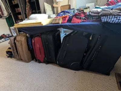 Assorted vintage and modern luggage, including rolling suitcases in black and red, and a tan hardside suitcase.