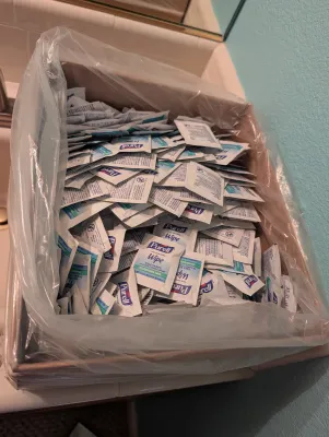 A large cardboard box lined with plastic and filled with individual Purell hand sanitizing wipe packets.