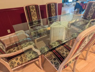 Postmodern dining set featuring a rectangular glass-top table on a travertine stone pedestal base, accompanied by six high-back chairs...