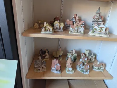 Collection of Lilliput Lane miniature cottages and buildings displayed on wooden shelves.