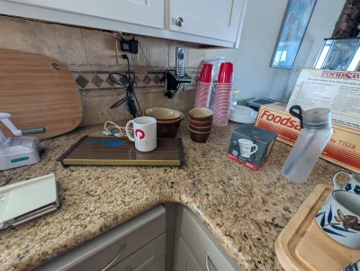 Assorted kitchenware including a vintage electric warming tray, ceramic mugs, mixing bowls, a spiralizer, and a FoodSaver vacuum sealer...