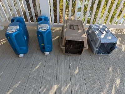 Two blue plastic Reliance Aqua-Tainer water containers alongside two plastic Kennel Cab II pet carriers in tan and grey, all showing...