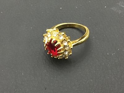 Sale Photo Thumbnail #274: Gold-tone costume jewelry cocktail ring featuring a prominent oval red central stone surrounded by a halo of clear rhinestone accents. Ring measures approximately size 8 on a ring mandrel. Good condition with minimal wear visible.