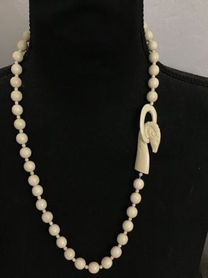 Sale Photo Thumbnail #137: A vintage cream-colored beaded necklace featuring a hand-carved focal element shaped like a ram or goat head hooked onto an oval loop. Made of carved bone, faux ivory, or composite resin beads strung together. Good condition with light vintage wear.
