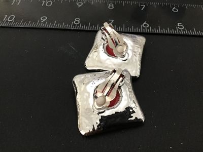 Sale Photo Thumbnail #36: Pair of bold retro-style square clip-on earrings featuring vibrant red enamel and a central domed cabochon set in silver-tone metal with a hammered back finish. Clip-on backs are functional and fitted with rubber comfort pads. Measure approximately 1.25 i