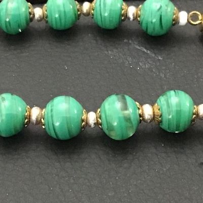 Sale Photo Thumbnail #65: Vintage beaded necklace featuring green striped art glass beads accented with brass filigree caps and small spacer beads. Measures approximately 22 inches end-to-end. Features a brass barrel screw clasp. Good vintage condition with light wear to metal acc