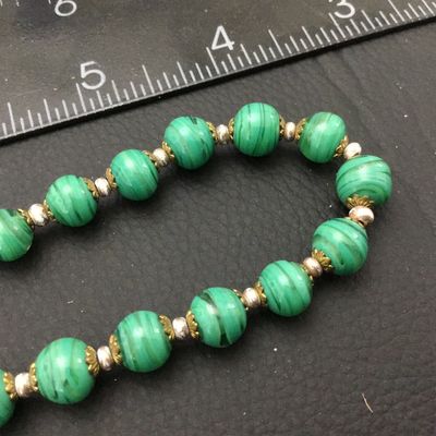 Sale Photo Thumbnail #67: Vintage beaded necklace featuring green striped art glass beads accented with brass filigree caps and small spacer beads. Measures approximately 22 inches end-to-end. Features a brass barrel screw clasp. Good vintage condition with light wear to metal acc