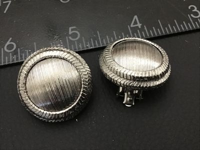 Sale Photo Thumbnail #244: Pair of vintage silver-tone clip-on earrings featuring a textured dome center and chevron patterned outer rim. Each clip-on earring measures approximately 1 inch in diameter. In good condition with functional clip backs and light vintage wear.