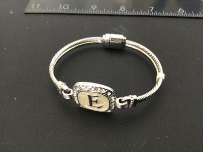 Sale Photo Thumbnail #31: Silver-tone twisted cable style cuff/bangle bracelet featuring a square center emblem with the initial 'E' set against an off-white enamel background, surrounded by a halo of clear rhinestones/crystals. Features a magnetic closure at the back. Light overa