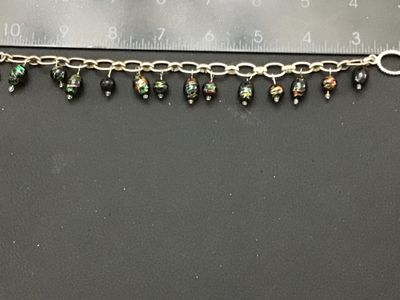 Sale Photo Thumbnail #256: A silver-tone chain bracelet featuring dangling black glass beads decorated with colorful metallic foil flecks/swirls in green, red, and gold tones. Features a textured toggle clasp closure. Measures approximately 7.5 to 8 inches in overall length. Good v