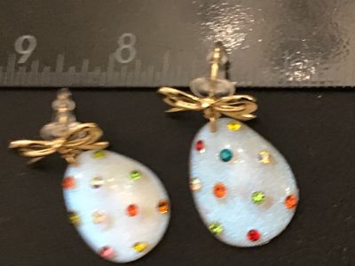 Sale Photo Thumbnail #282: Pair of festive  egg dangle earrings featuring iridescent white glittery teardrop/egg-shaped bases accented with multicolored rhinestones. Topped with gold-tone ribbon bows and post backs with plastic bullet clutch stoppers. Measures approximately 1.5 inc