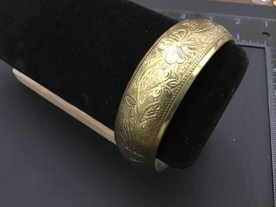 Sale Photo Thumbnail #219: A vintage gold-tone brass bangle bracelet featuring an intricate embossed floral and leaf design with textured background details. Inner diameter measures approximately 2.5 inches across. Shows minor age-appropriate wear and light patina.