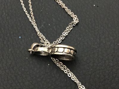 Sale Photo Thumbnail #164: A sterling silver chain necklace featuring an oval-cut faceted dark red stone (possibly garnet) pendant with a small accent stone setting above it. The pendant loop is marked 'LUC' and features textured dot details along the side setting. Includes a delic