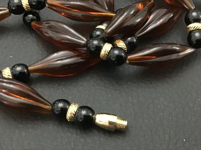 Sale Photo Thumbnail #172: Long vintage beaded strand necklace featuring amber-toned fluted/marquise acrylic beads alternating with black round beads and textured gold-tone spacers. Features a threaded barrel clasp closure. Measures approximately 30+ inches in length. In good vinta