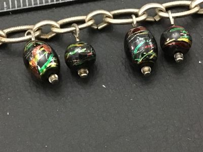 Sale Photo Thumbnail #258: A silver-tone chain bracelet featuring dangling black glass beads decorated with colorful metallic foil flecks/swirls in green, red, and gold tones. Features a textured toggle clasp closure. Measures approximately 7.5 to 8 inches in overall length. Good v