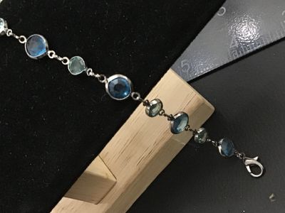 Sale Photo Thumbnail #283: A silver-tone link station bracelet featuring alternating round bezel-set faceted crystals in dark blue and light green hues. The bracelet measures approximately 7.5 inches long and fastens with a lobster claw clasp. In good pre-owned condition with light
