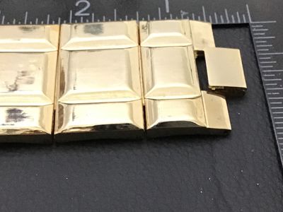 Sale Photo Thumbnail #235: A vintage gold-tone fashion watch featuring a wide, geometric segmented link band and a small square dark dial with stylized graphic logo and minimalist hour markers. Measures Workingapproximately 7.5 to 8 inches in total length. Stainless steel or metal 