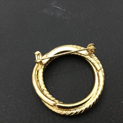 Sale Photo Thumbnail #91: Gold-tone circular brooch featuring a classic twisted rope motif interwoven with a smooth polished ring. Features a standard pin back with a safety clasp. Appears to be in very good vintage condition with minor surface wear typical of age.