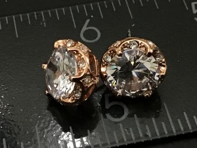 Sale Photo Thumbnail #248: Pair of rose gold tone stud earrings featuring large faceted clear central crystals/rhinestones with halo accents. Each earring measures approximately 1/2 inch in diameter. Includes post backs. In good condition with bright sparkle and light wear consiste