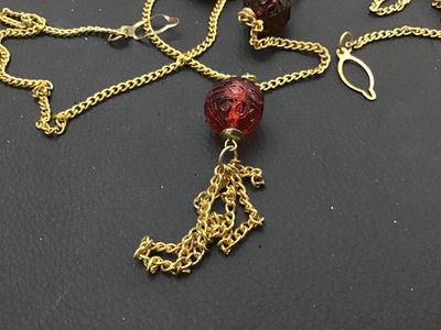 Sale Photo Thumbnail #211: Vintage gold-tone chain necklace featuring carved translucent red glass beads and a small metal chain tassel pendant. Has a hook and eye/ring clasp. In good vintage condition with minor surface wear consistent with age.