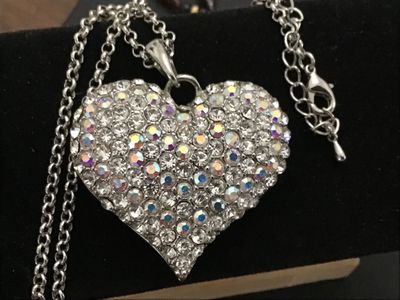 Sale Photo Thumbnail #154: A silver-tone chain necklace featuring a large heart-shaped pendant encrusted with clear and aurora borealis pave rhinestones. The back of the pendant features a openwork filigree heart pattern. Features an adjustable rolo chain with a lobster claw clasp.