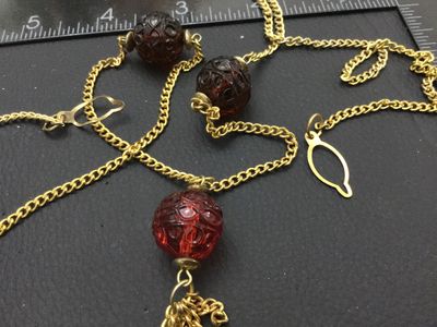 Sale Photo Thumbnail #212: Vintage gold-tone chain necklace featuring carved translucent red glass beads and a small metal chain tassel pendant. Has a hook and eye/ring clasp. In good vintage condition with minor surface wear consistent with age.