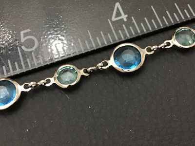Sale Photo Thumbnail #285: A silver-tone link station bracelet featuring alternating round bezel-set faceted crystals in dark blue and light green hues. The bracelet measures approximately 7.5 inches long and fastens with a lobster claw clasp. In good pre-owned condition with light
