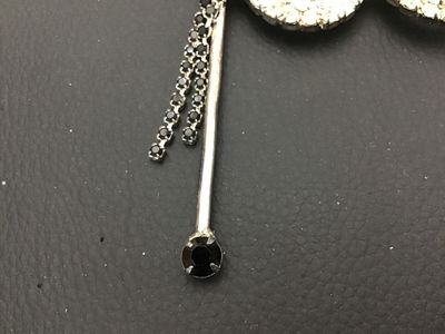 Sale Photo Thumbnail #128: Vintage silver-tone rhinestone brooch shaped like a masquerade opera mask on a stick. Features clear set rhinestones across the mask frame with black rhinestone accents along the handle and dangling fringe details. Secure pin back fastener. Shows light vi