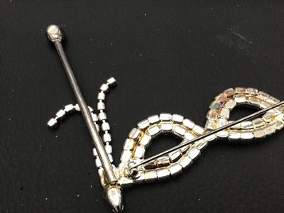 Sale Photo Thumbnail #129: Vintage silver-tone rhinestone brooch shaped like a masquerade opera mask on a stick. Features clear set rhinestones across the mask frame with black rhinestone accents along the handle and dangling fringe details. Secure pin back fastener. Shows light vi