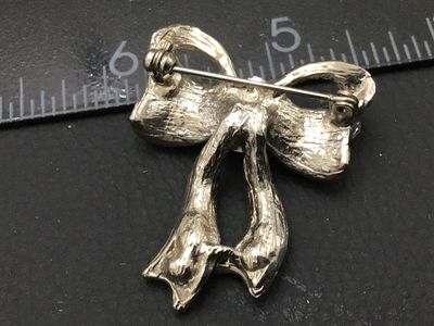 Sale Photo Thumbnail #276: A silver-tone ribbon bow brooch featuring iridescent/aurora borealis and clear rhinestones with pink rhinestone accent stones at the center knot. Measures approximately 1.25 inches across. Features a roll-over safety pin clasp on the back. Good pre-owned 
