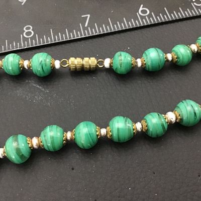 Sale Photo Thumbnail #66: Vintage beaded necklace featuring green striped art glass beads accented with brass filigree caps and small spacer beads. Measures approximately 22 inches end-to-end. Features a brass barrel screw clasp. Good vintage condition with light wear to metal acc