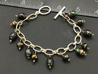 Sale Photo Thumbnail #255: A silver-tone chain bracelet featuring dangling black glass beads decorated with colorful metallic foil flecks/swirls in green, red, and gold tones. Features a textured toggle clasp closure. Measures approximately 7.5 to 8 inches in overall length. Good v